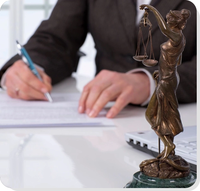 A person is writing on paper near a statue of lady justice.