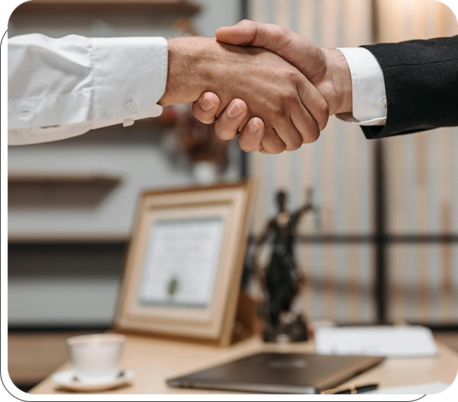 Two people shaking hands over a desk.